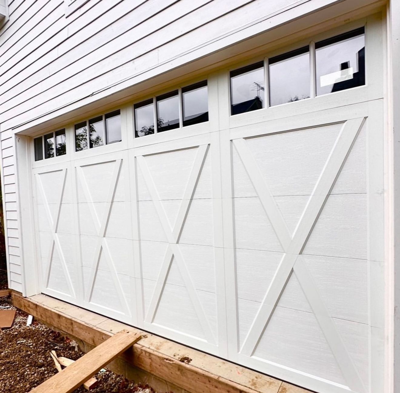 White garage door with cross design and small rectangular windows on a white house.