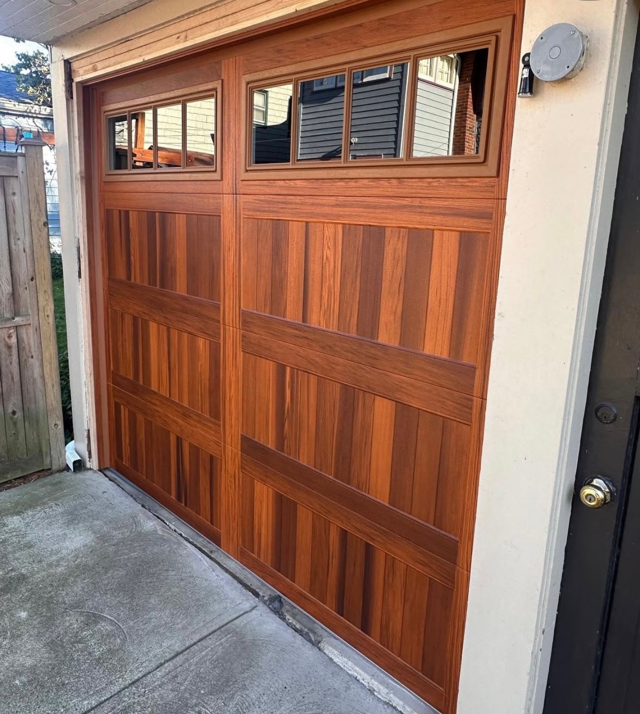 Wooden garage door with glass windows, reddish-brown vertical planks, cream trim, and a concrete surface.