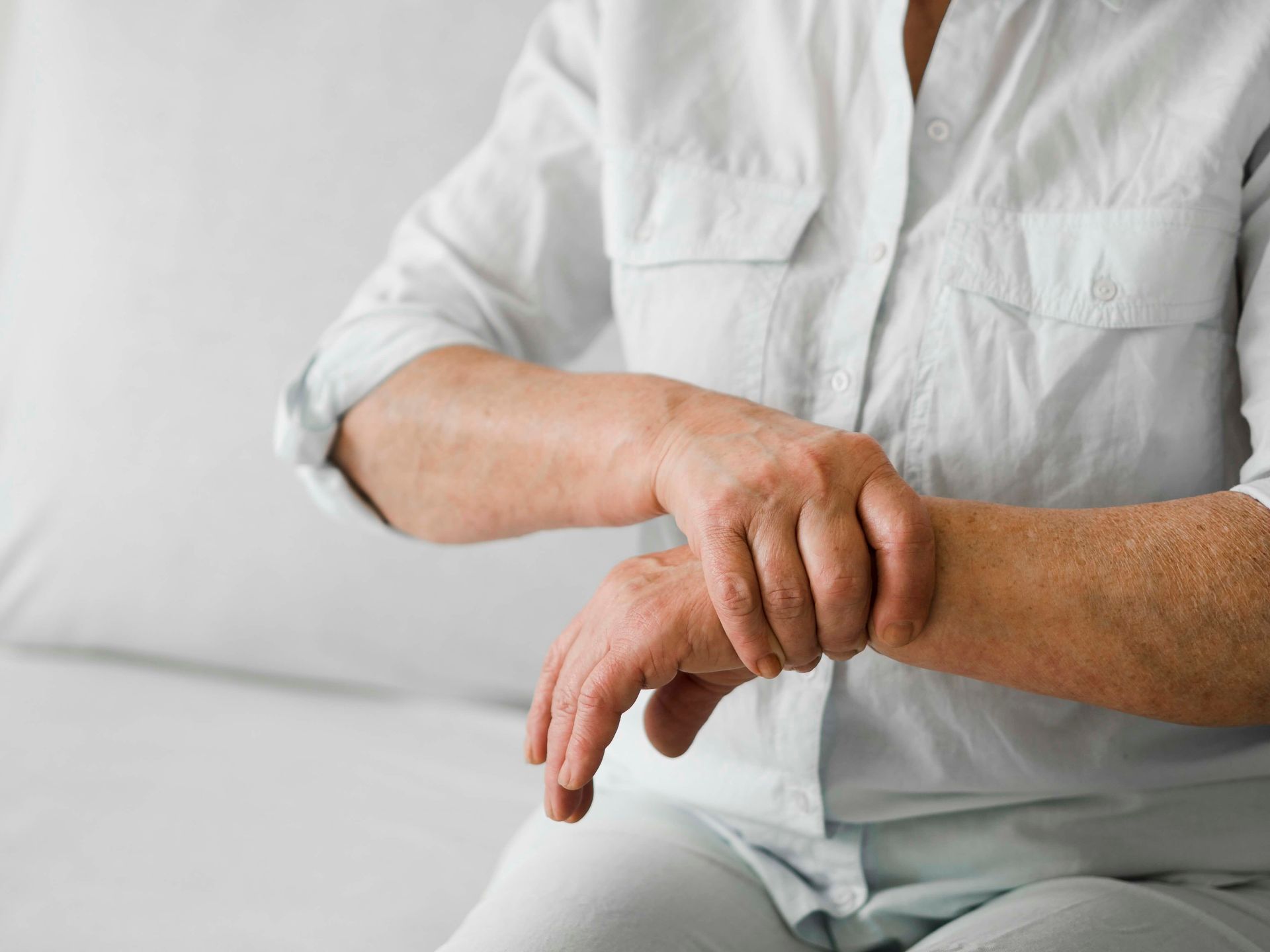 an elderly woman is sitting on a couch holding her wrist in pain .