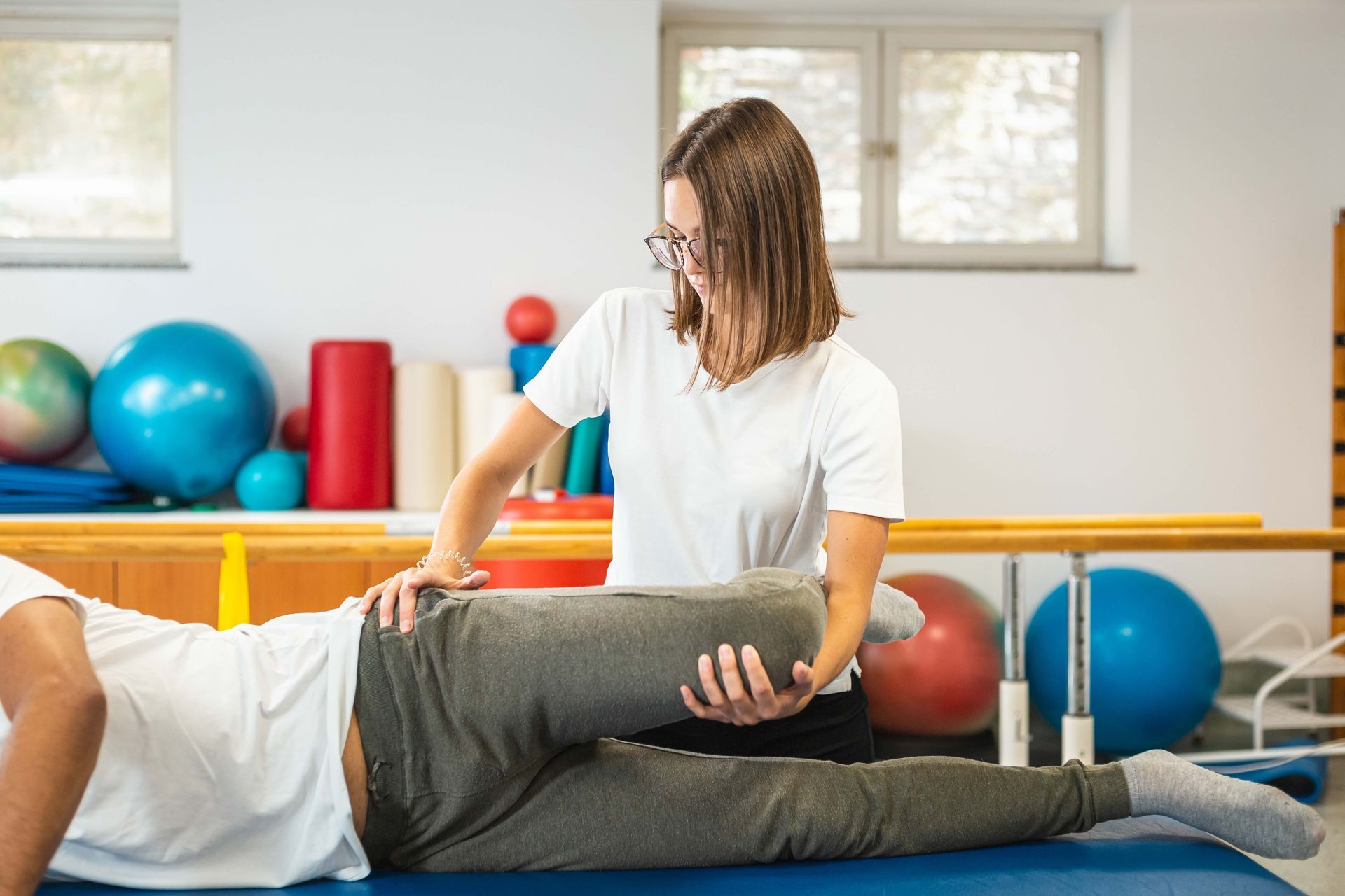 a woman is stretching a man 's leg in a gym .