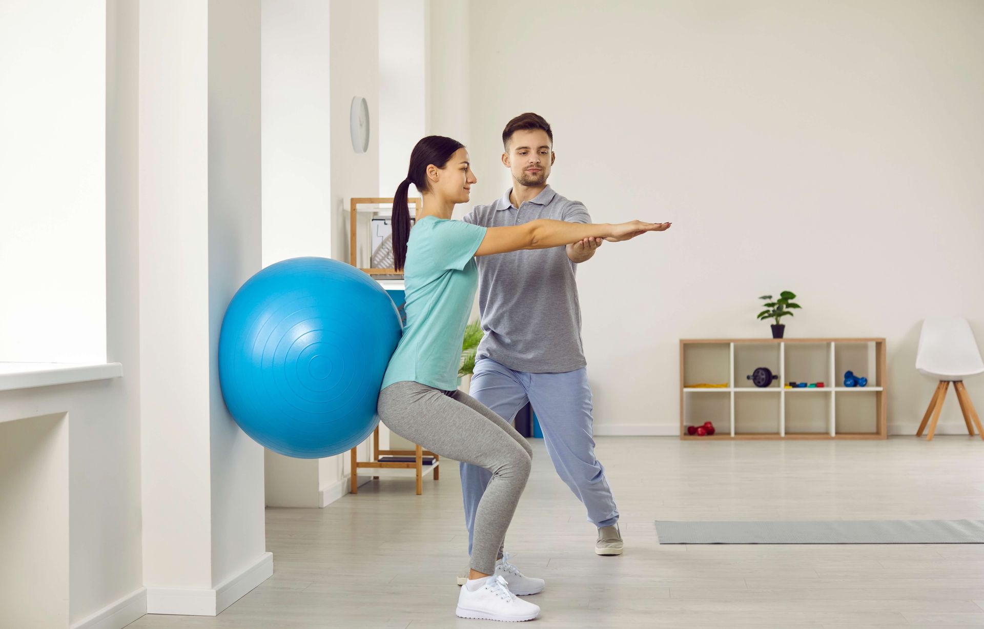 a man and a woman are doing squats with a blue exercise ball .