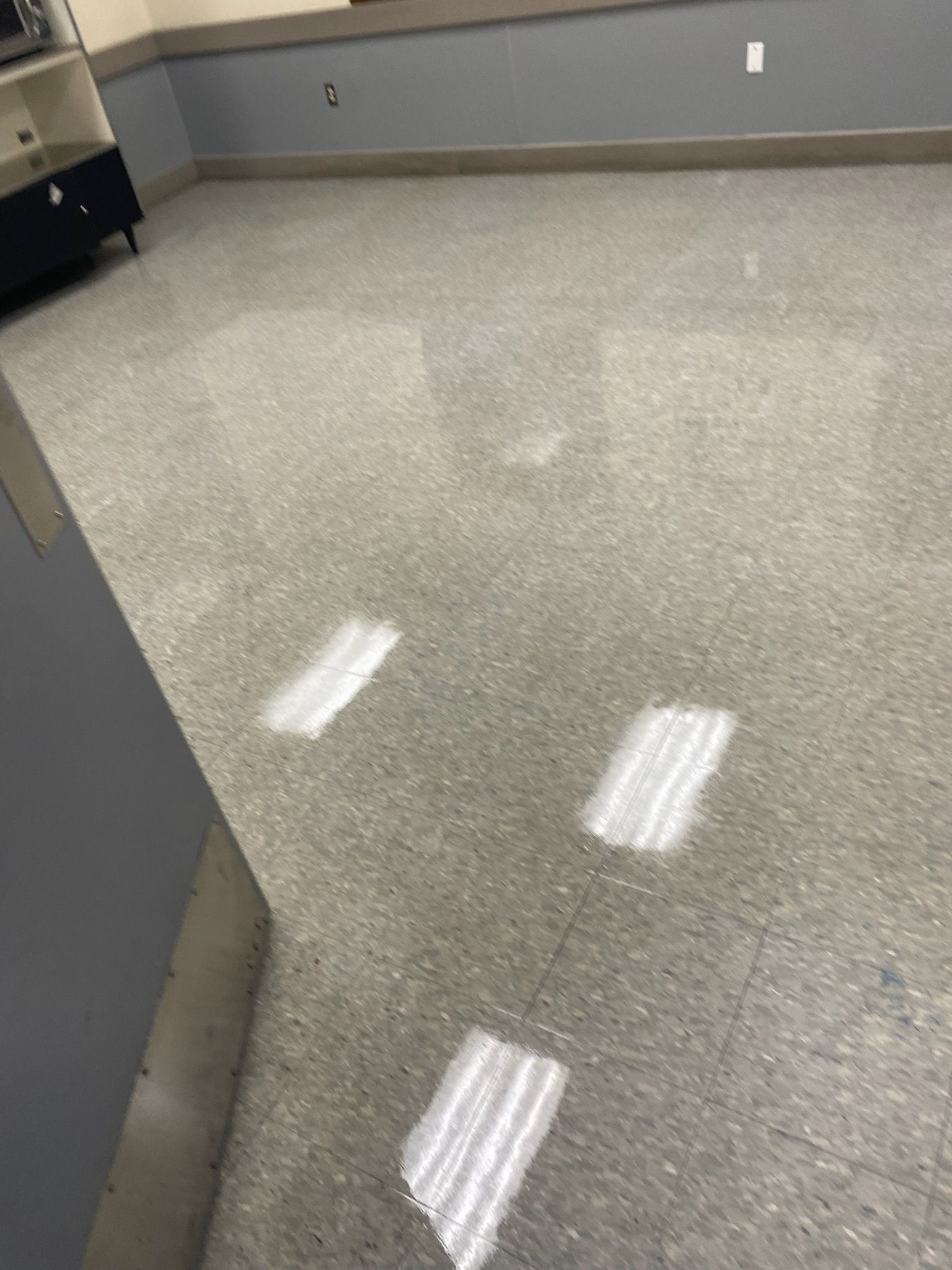 Shiny speckled gray floor in an empty indoor room with reflections of overhead lights
