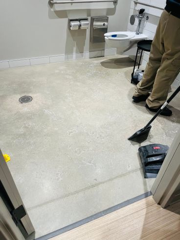 Small bathroom with sink and toilet; person sweeping the floor with a dustpan nearby.