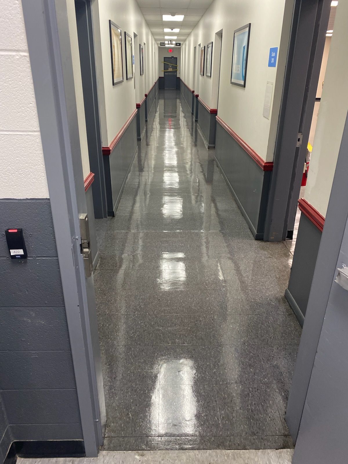Empty office hallway with gray walls, glossy floor, and framed pictures on both sides.