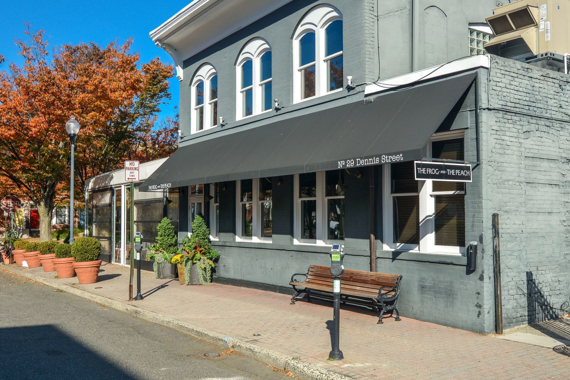 Gray building with black awning, windows, and bench on sidewalk; autumn trees and clear sky. Visit our convenient downtown Brunswick location, where you're surrounded by shopping, dining, and local attractions. Start living better at The Brunswick apartments in downtown Brunswick, NJ. 
