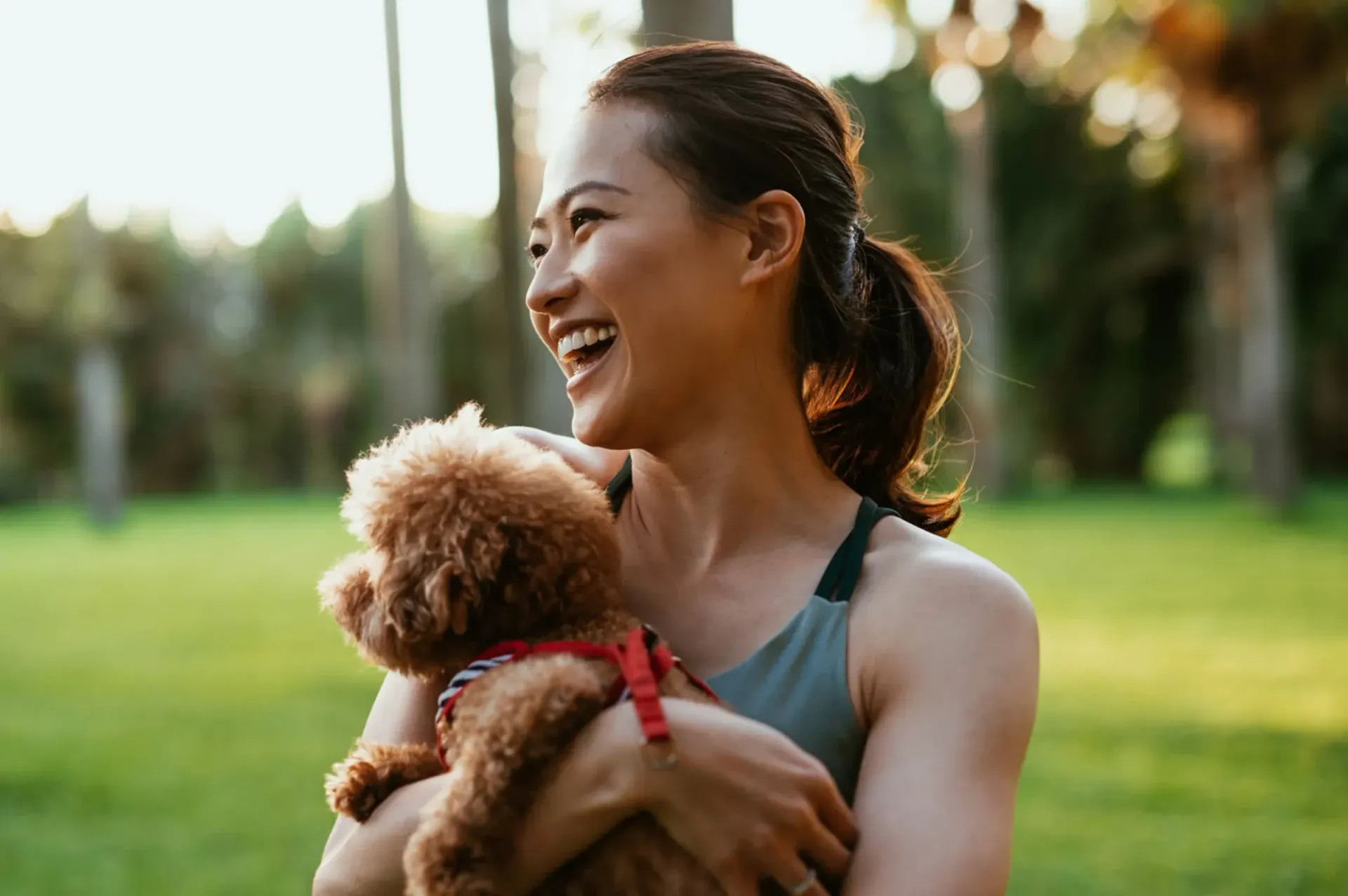 Woman in a park, laughing and holding her small dog. 