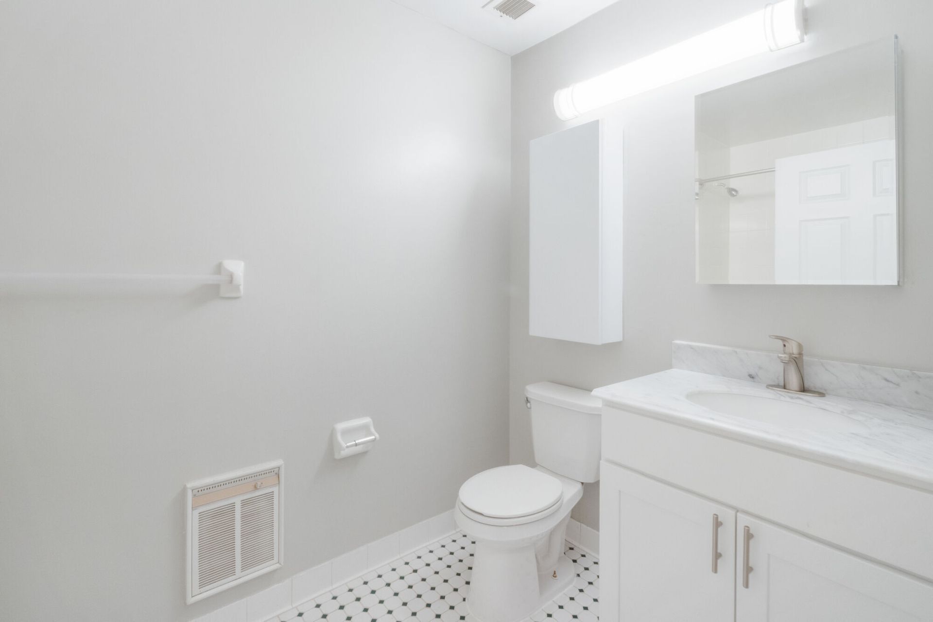 Bathroom with white fixtures, light gray walls, and black and white tiled floor. Make The Brunswick your home today! Contact us to schedule a tour of our studio, 1, and 2-bedroom New Brunswick apartments for rent. 
