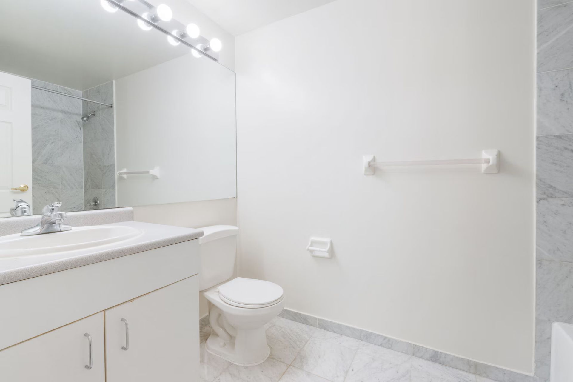 White bathroom with toilet, vanity, large mirror, and towel rack. Make The Brunswick your home today! Contact us to schedule a tour of our studio, 1, and 2-bedroom New Brunswick apartments for rent. 