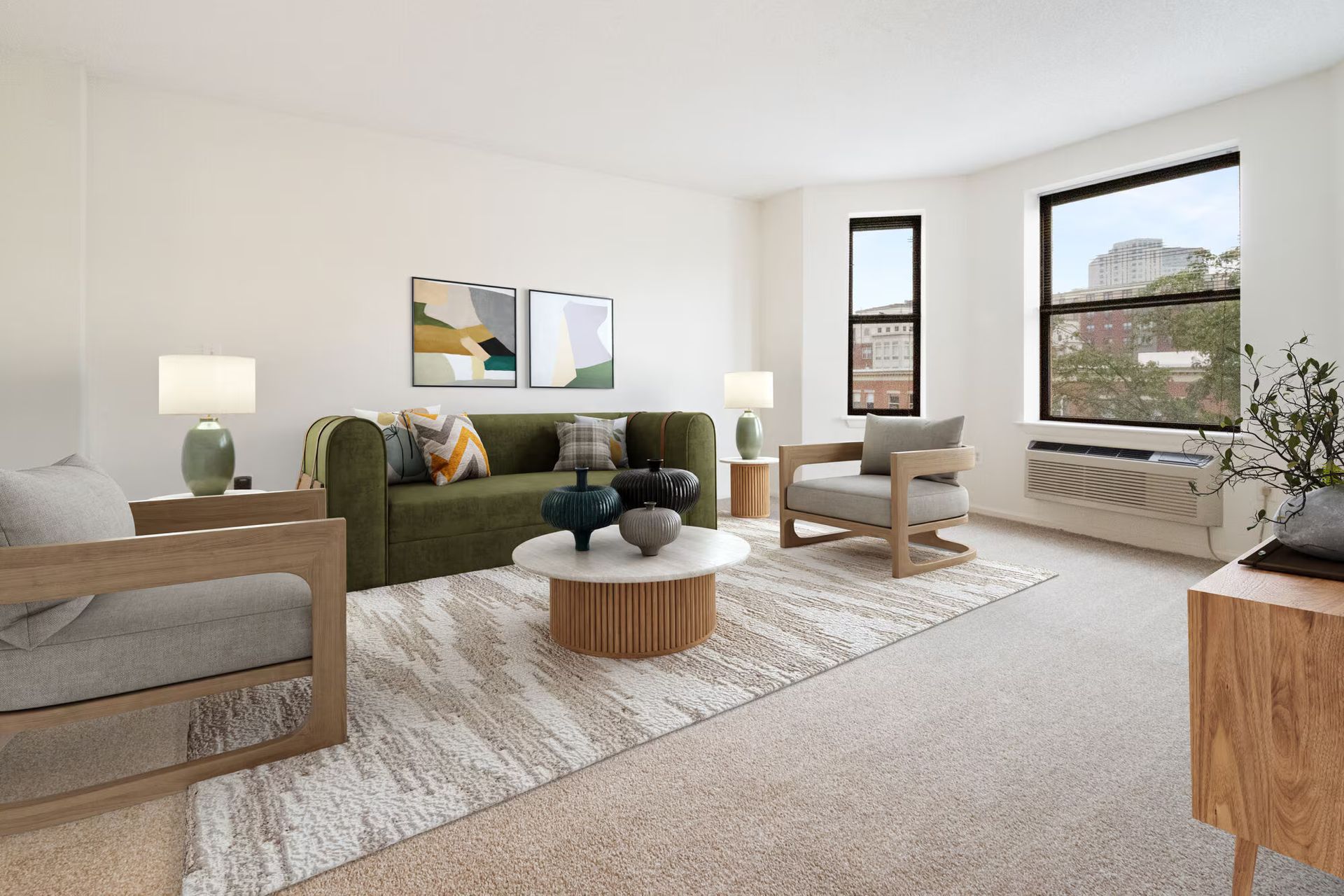 Living room with neutral tones: green sofa, wooden chairs, round coffee table, and large window. Contact us to take a tour of our studio, 1, and 2-bedroom apartments for rent in New Brunswick, NJ today!