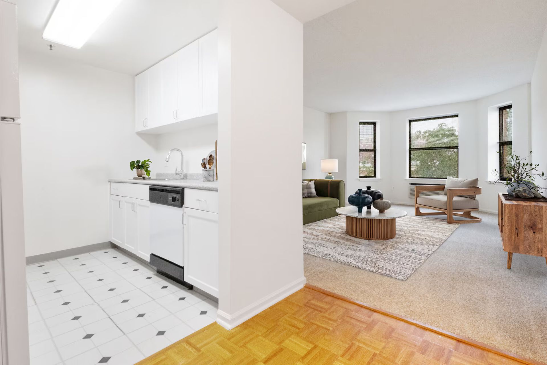 Bright, white apartment interior with kitchen, living room with green sofa, and hardwood floor entrance. Tour our spacious studio, 1, and 2-bedroom apartments for rent in New Brunswick, NJ today!
