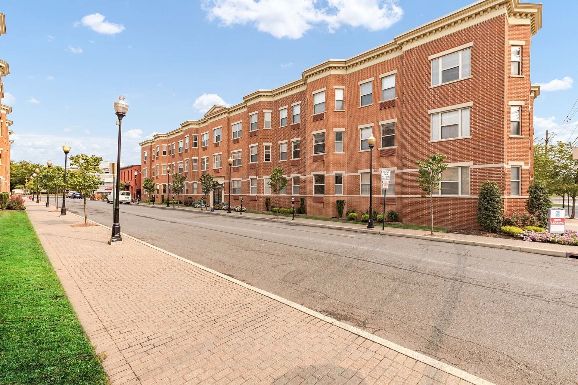 Brick apartment building on a street with trees, lampposts, and a grassy area. Blue sky with clouds. Visit our convenient downtown Brunswick location, where you're surrounded by shopping, dining, and local attractions. Start living better at The Brunswick apartments in downtown Brunswick, NJ. 