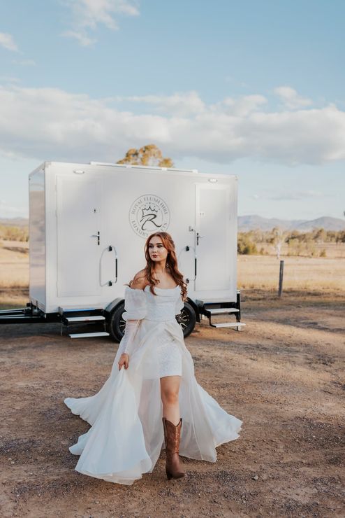 a woman in a wedding dress and cowboy boots stands in front of a trailer