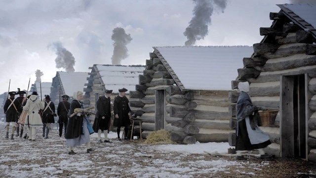 groups of soldiers standing outside of snow covered log cabins from the revolutionary war at valley forge historical park in valley forge, pa