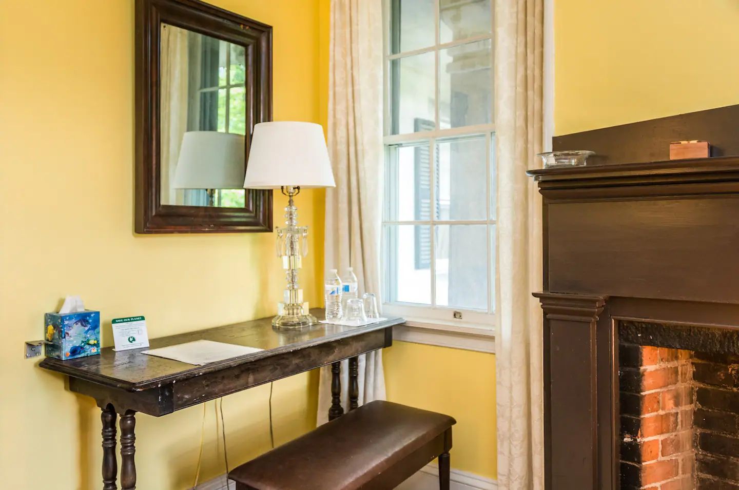 A room with a desk , lamp , mirror and fireplace.