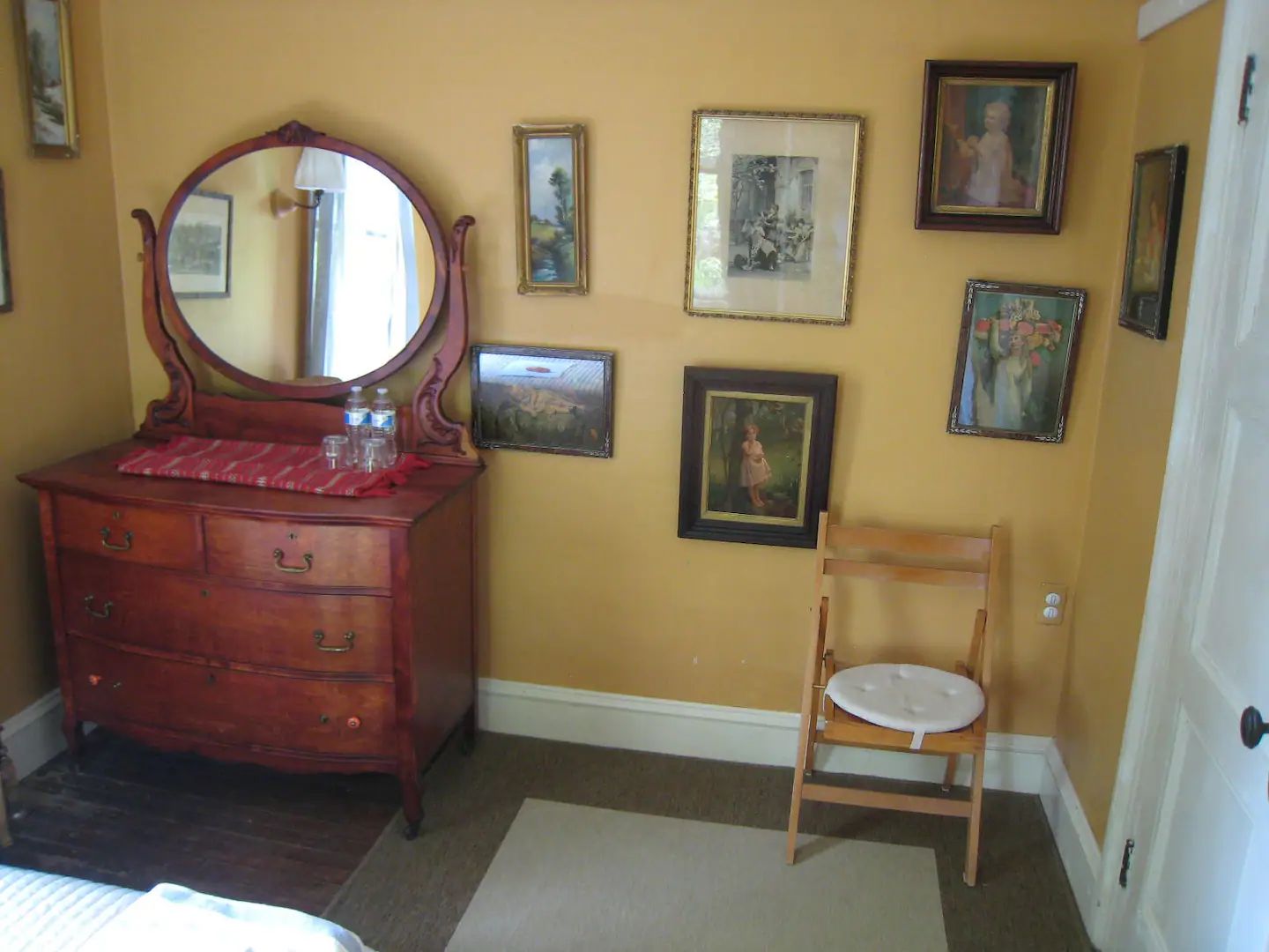 A bedroom with a dresser and a chair with pictures on the wall