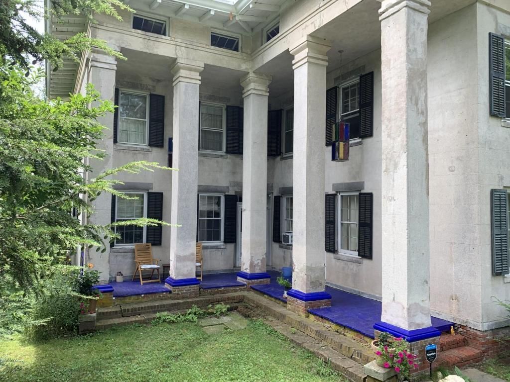 A large white house with columns and black shutters has a large porch.