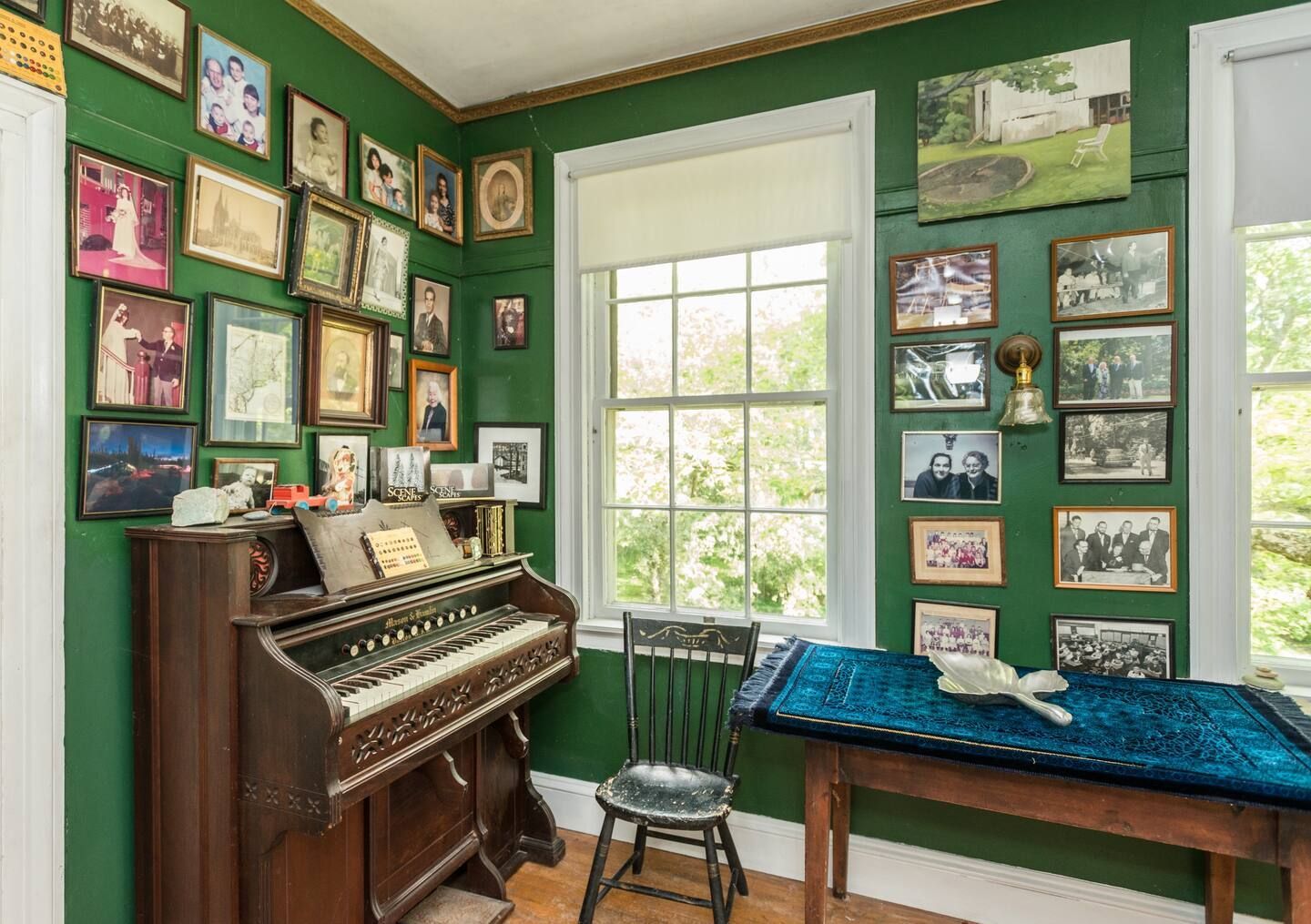 A room with a piano , chair , table and pictures on the wall.