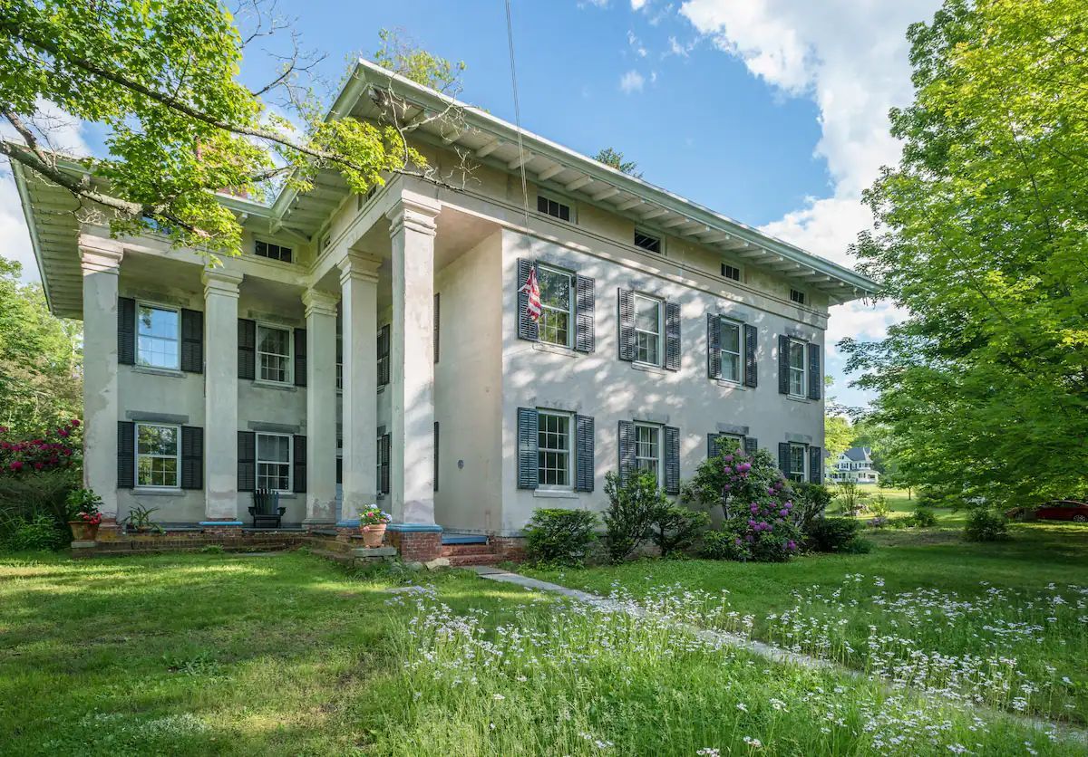 A large white house with a lot of windows is surrounded by trees and grass.