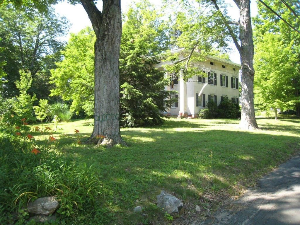 A large white house is surrounded by trees and grass