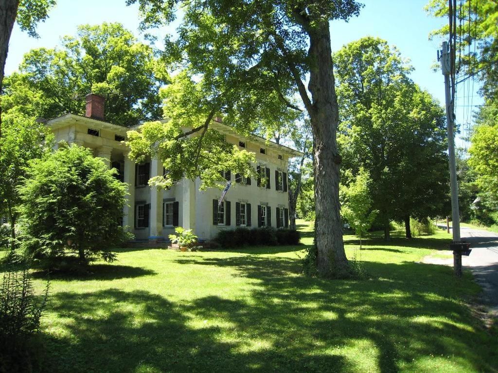 A large white house is surrounded by trees and grass