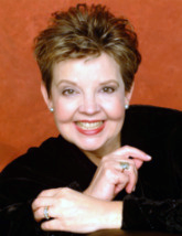 A woman with short hair and a ring on her finger smiles for the camera