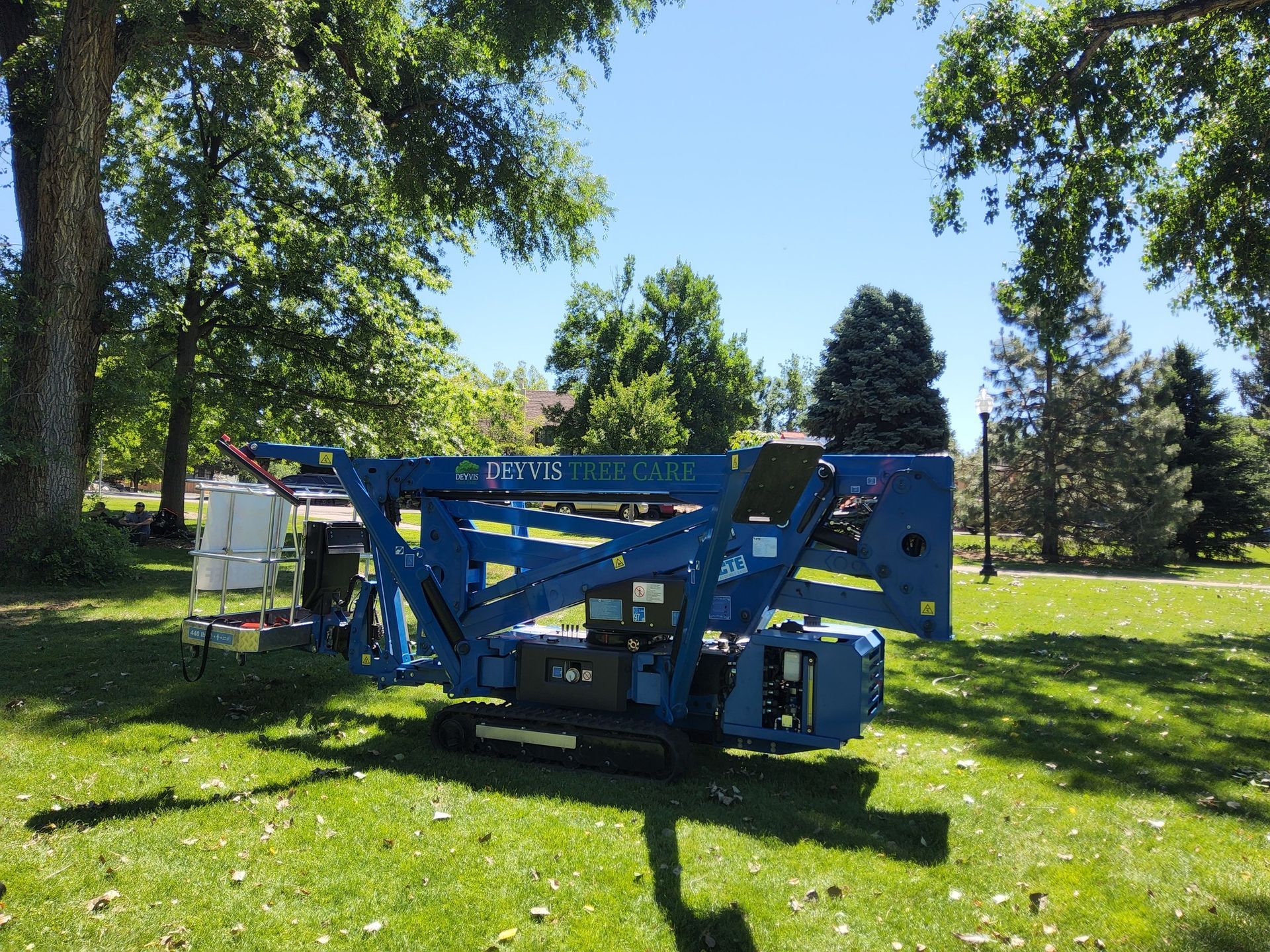 Blue lift equipment on green grass in a park. Trees and blue sky in background.