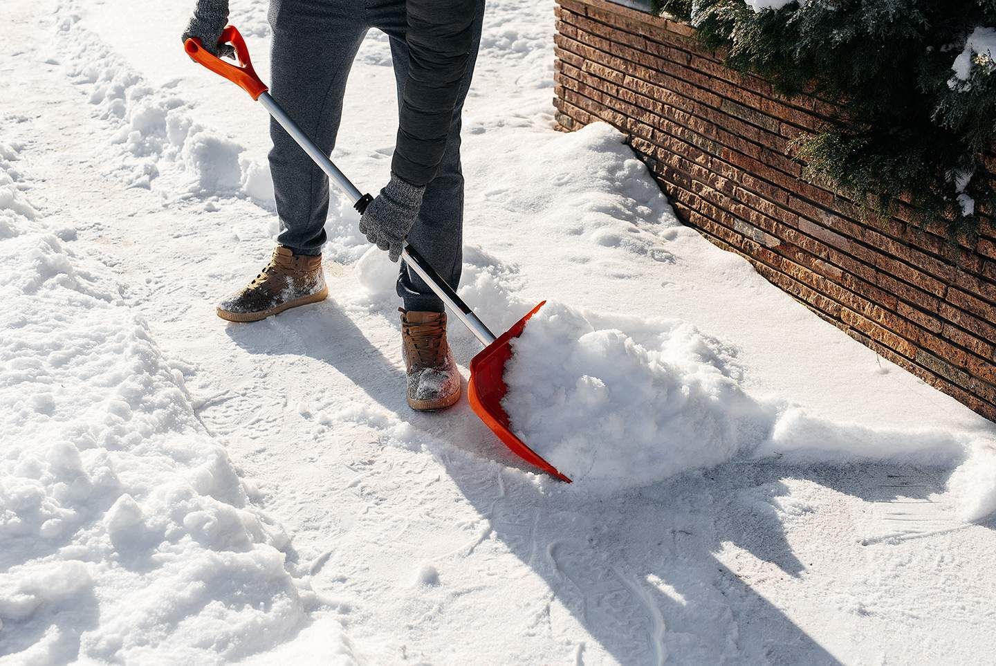 Person shoveling snow on a snowy walkway, using a red shovel.