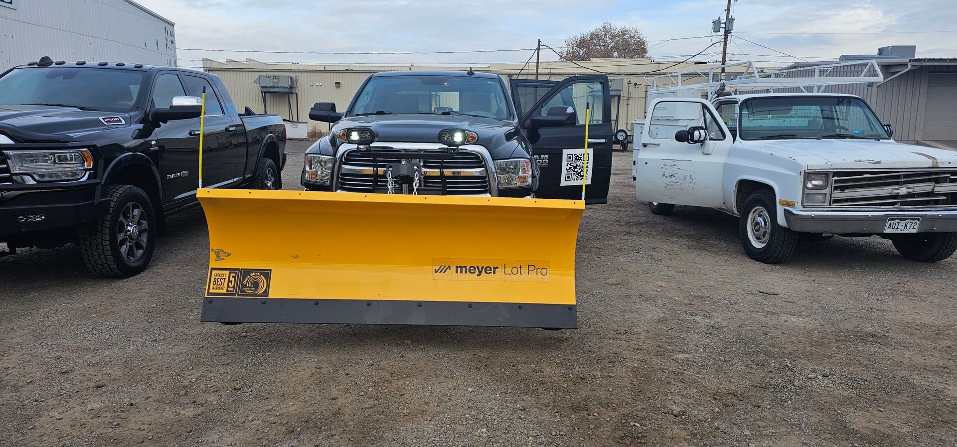 A group of snow plows are parked next to each other in a gravel lot.