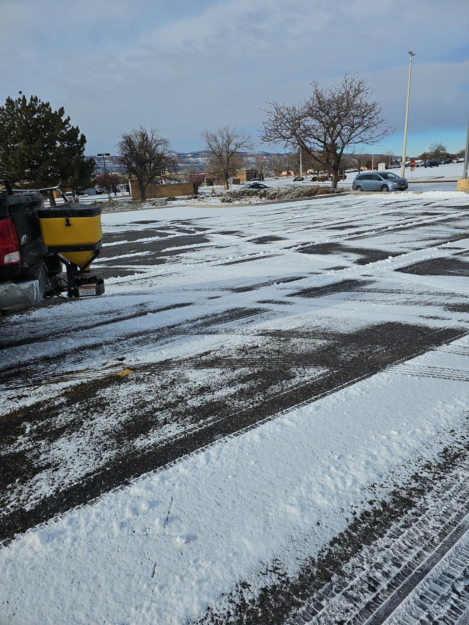 A snow plow is spreading snow on a parking lot.