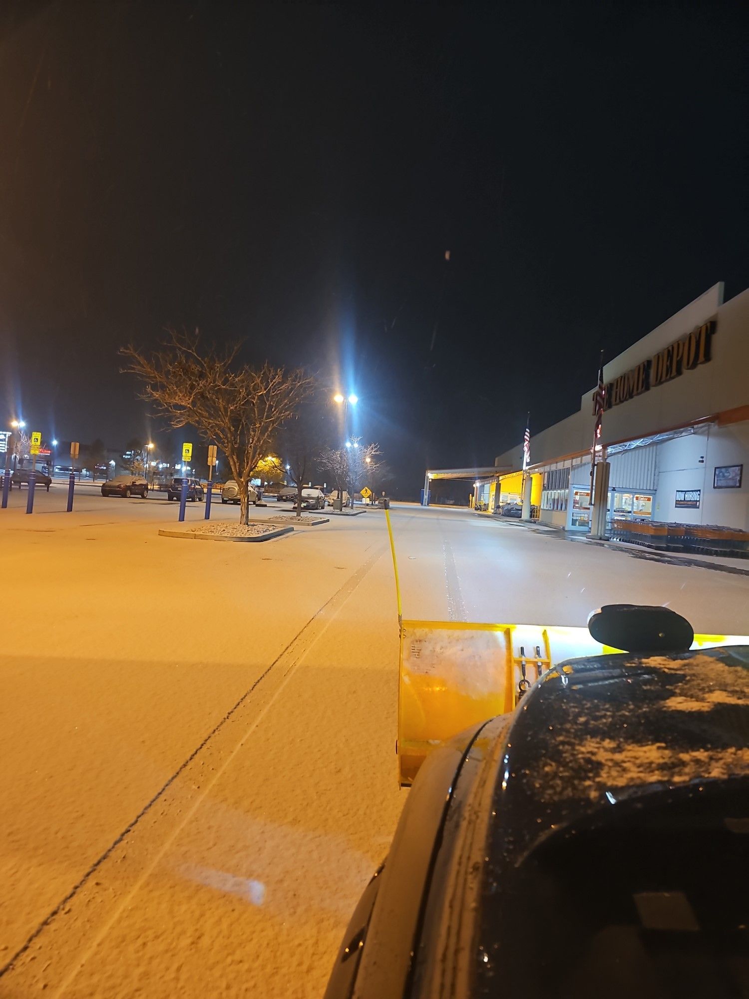 A snow plow is parked in front of a store at night