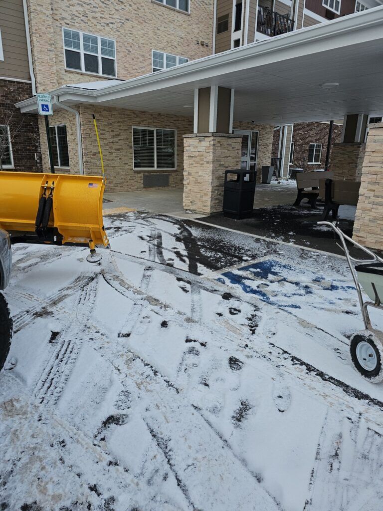 A snow plow is parked in the snow in front of a building.