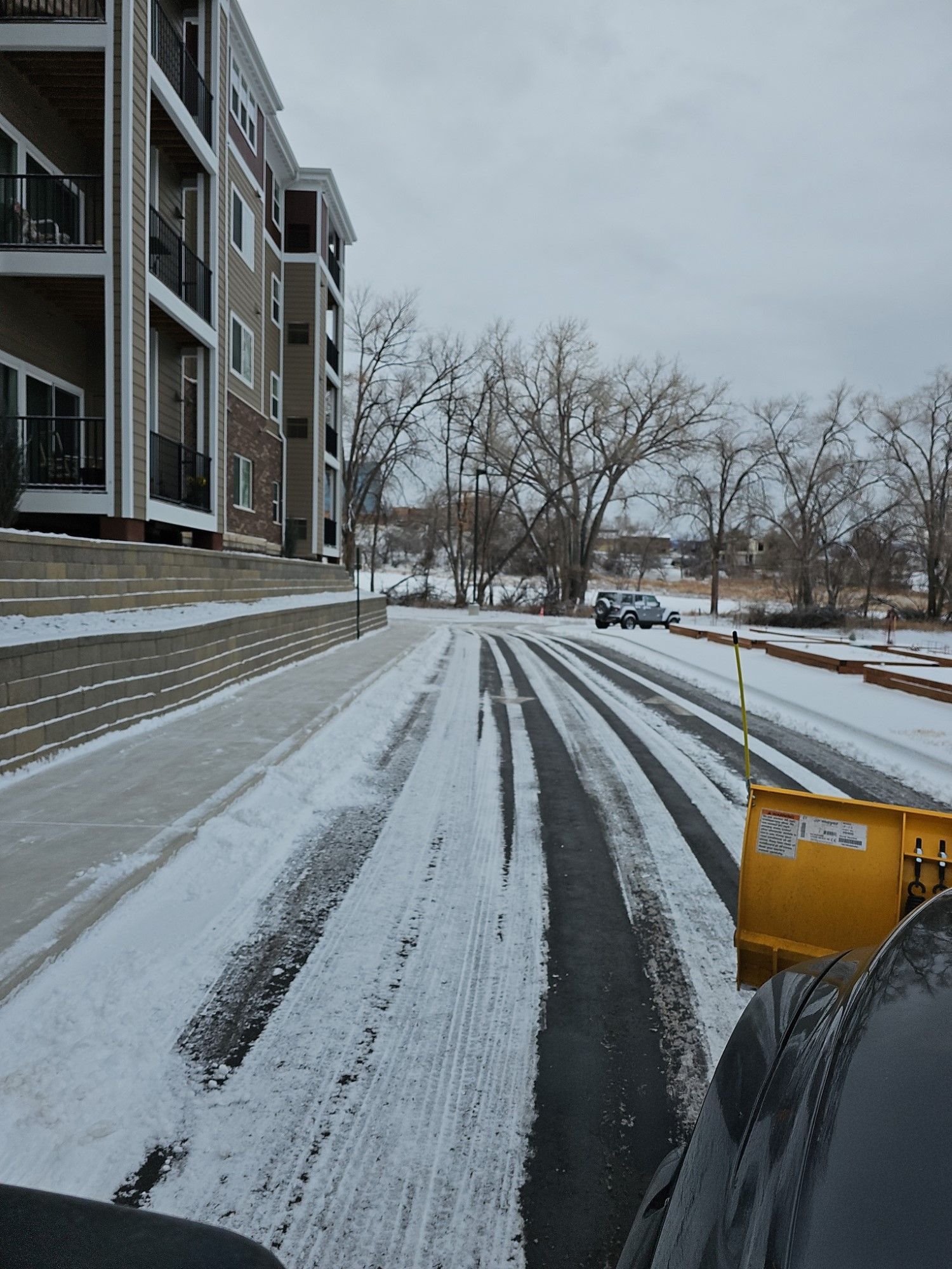 A snow plow is clearing a snowy street in front of a building.