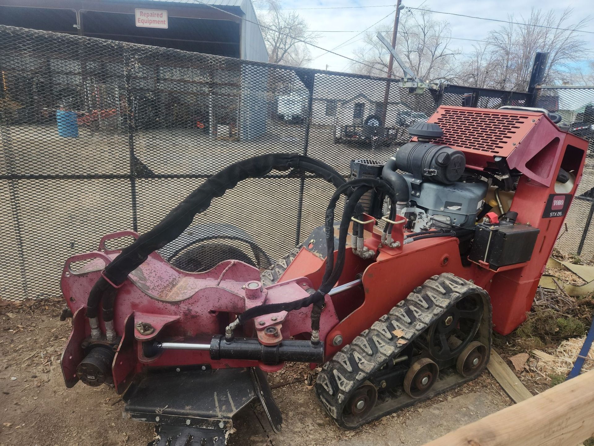 A red tractor is parked in front of a chain link fence.