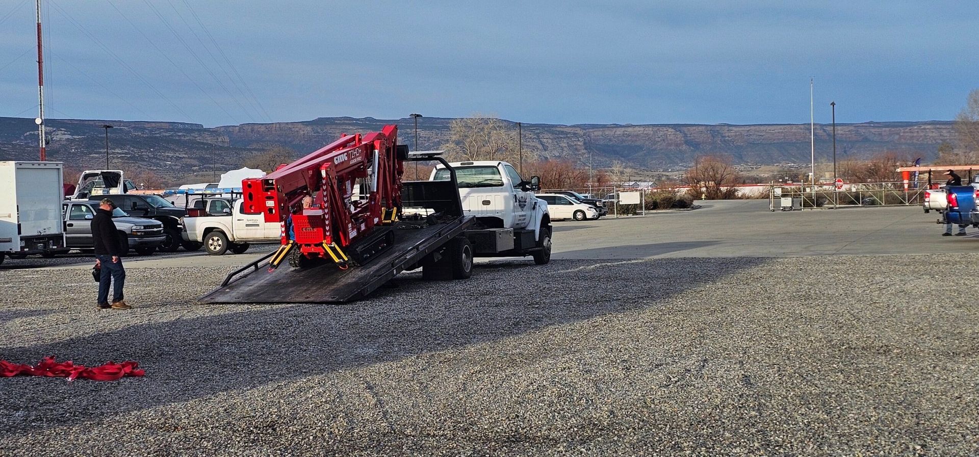 A red crane is being towed by a truck in a gravel lot.