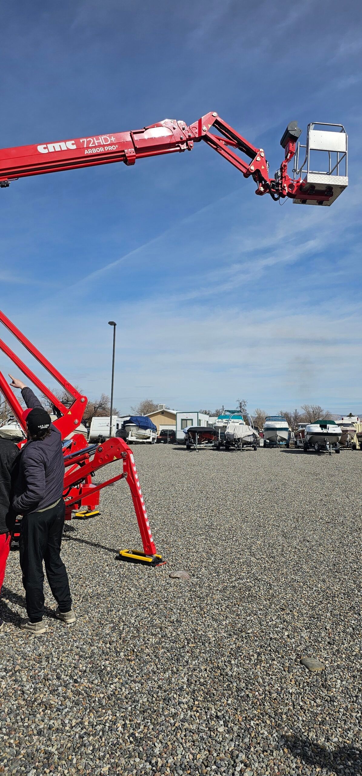A man is standing next to a red crane in a gravel lot.