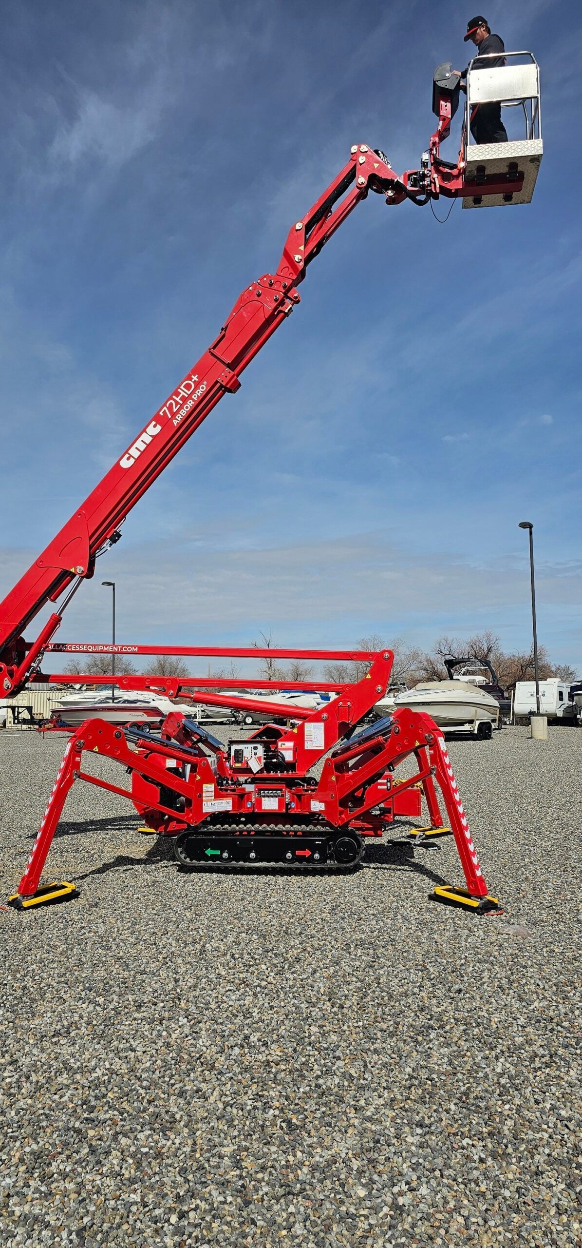 A red spider lift is sitting on top of a gravel lot.