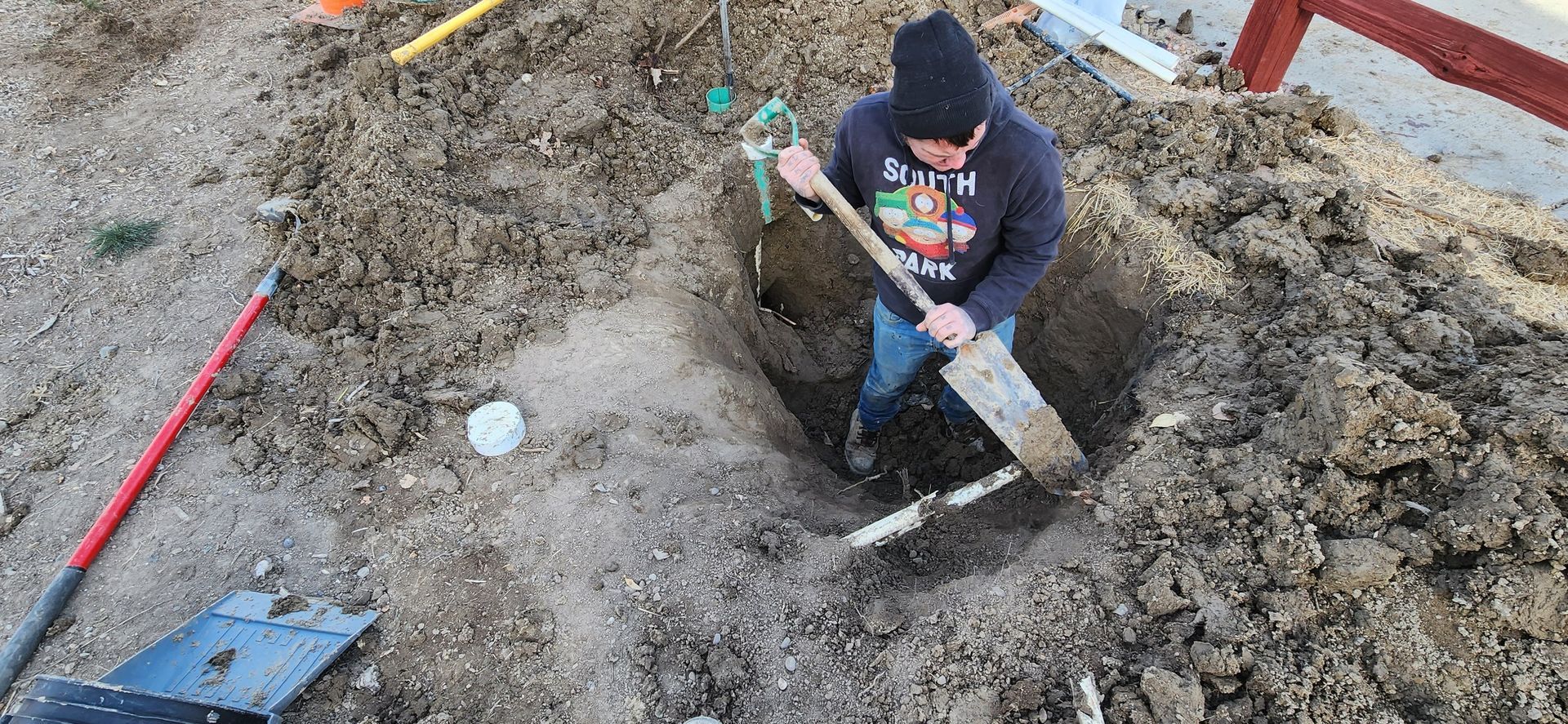 A man is digging a hole in the dirt with a shovel.