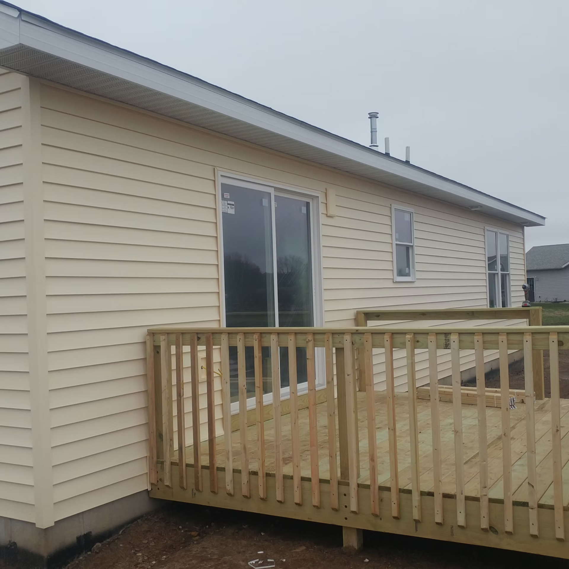 Beige house exterior with sliding glass door and small wooden deck under cloudy sky