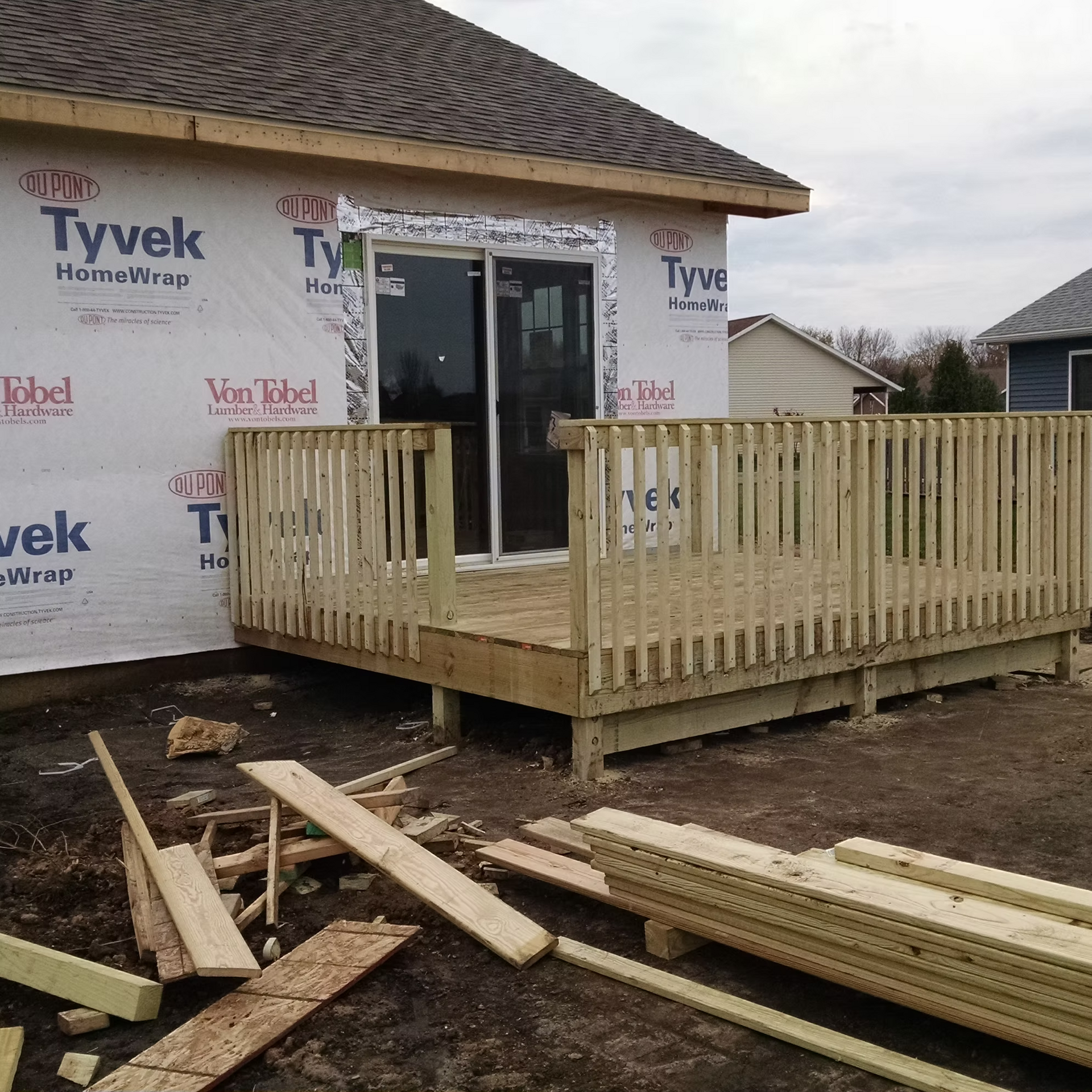 House under construction with Tyvek wrap and a wooden deck and railing in front