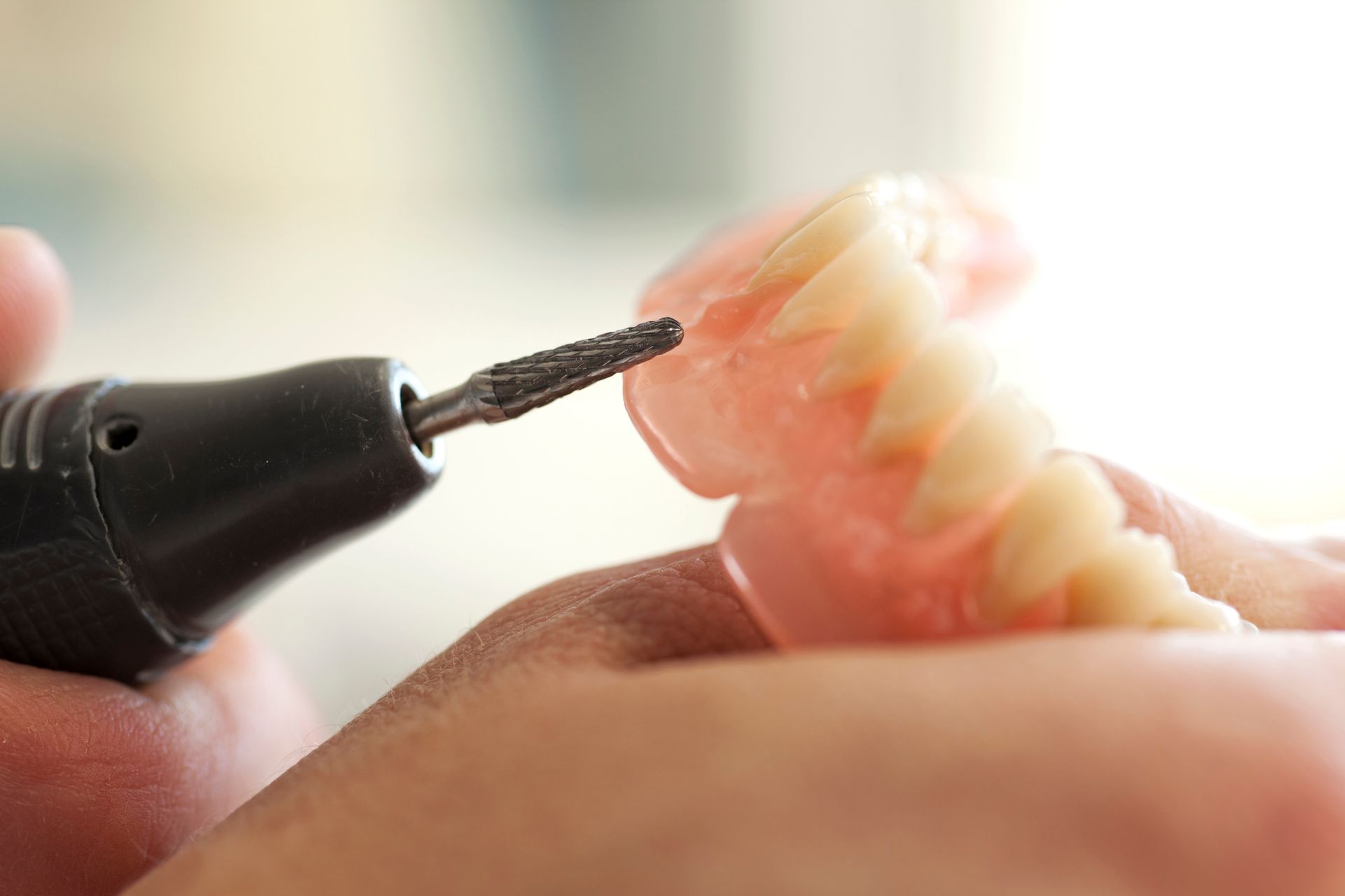 A person is grinding a denture with a grinder.