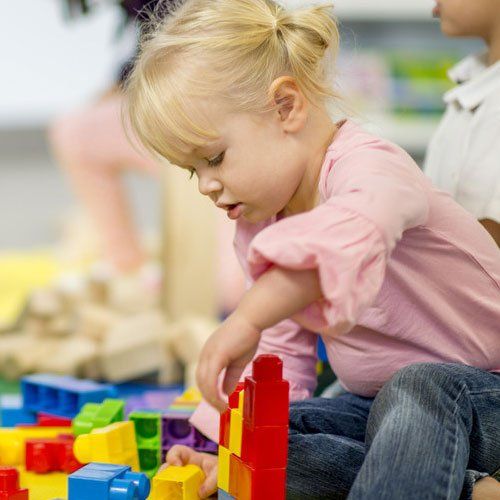 A little girl in a pink top and jeans playing with brightly coloured blocks
