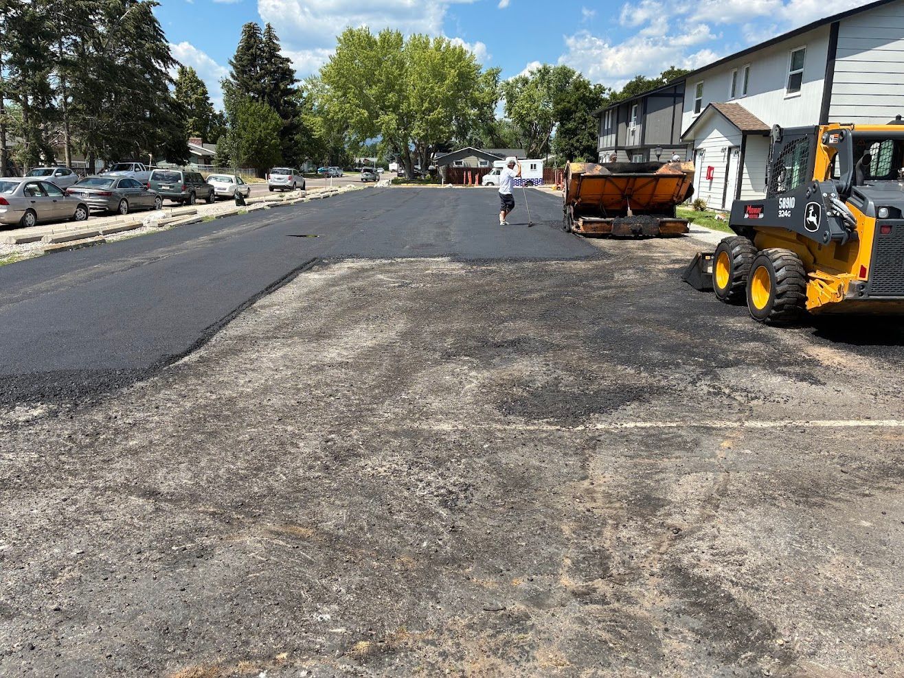 Yellow and black road roller compacting asphalt on a street; a person in red pants operates it.