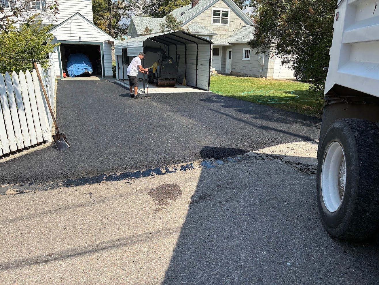 Workers in red coveralls paving asphalt on a road, smoke rising.