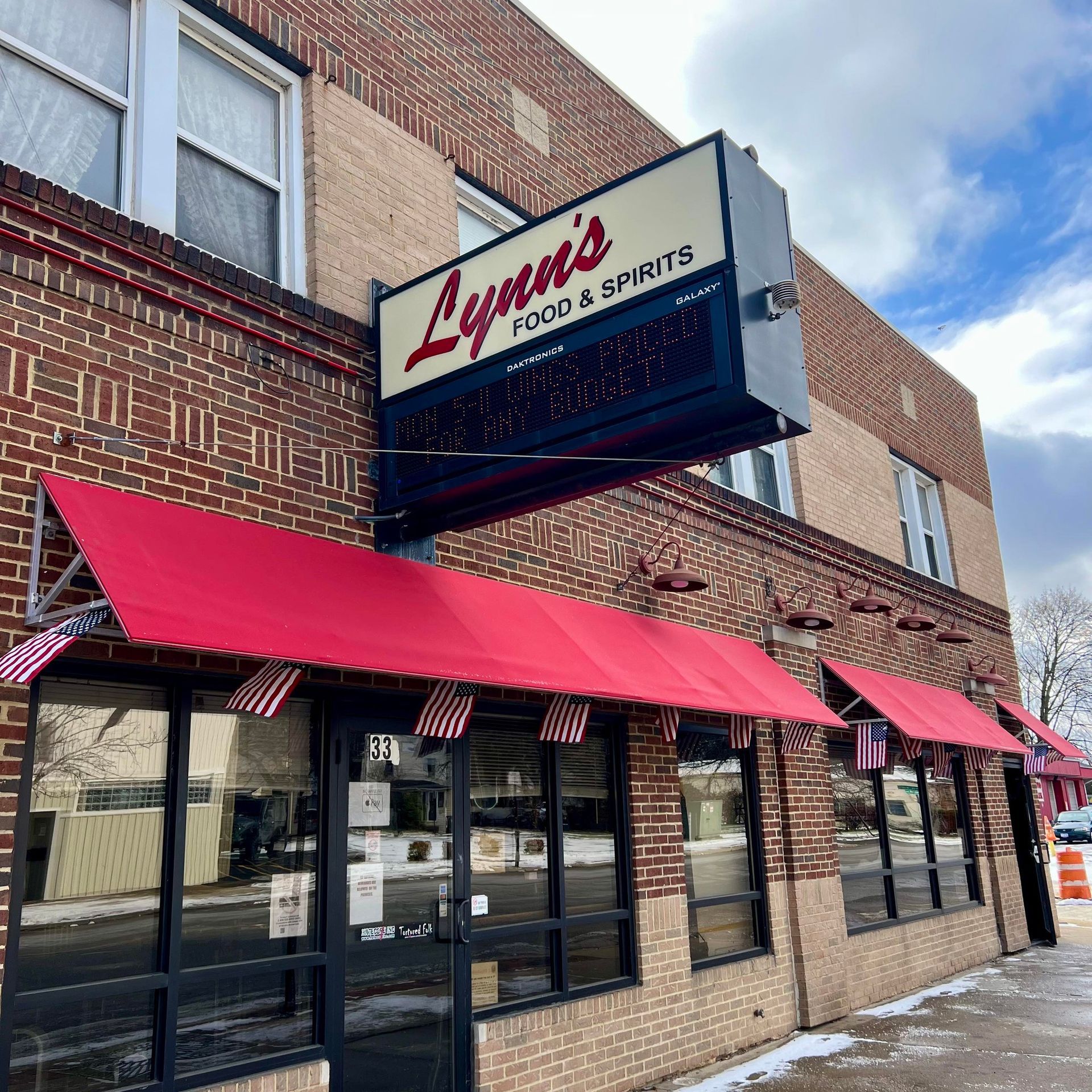 Lynn's Food & Spirits, brick building with red awnings and sign, windows, snow on sidewalk.