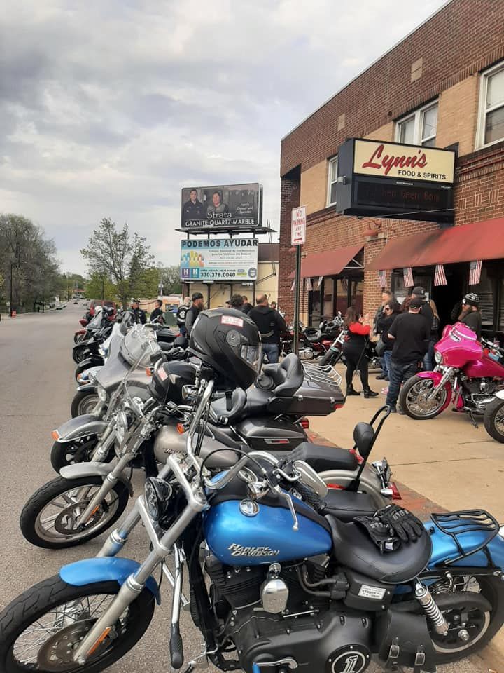 Motorcycles parked in front of a bar, people standing nearby.