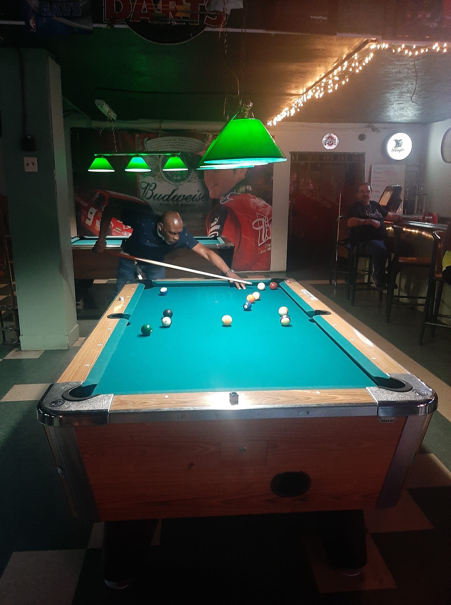 Man shooting pool in a bar, focused, cue stick in hand. Green felt table, overhead lighting, dim setting.