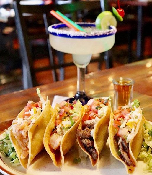 Tacos on a plate with margarita and shot glass on wooden table.