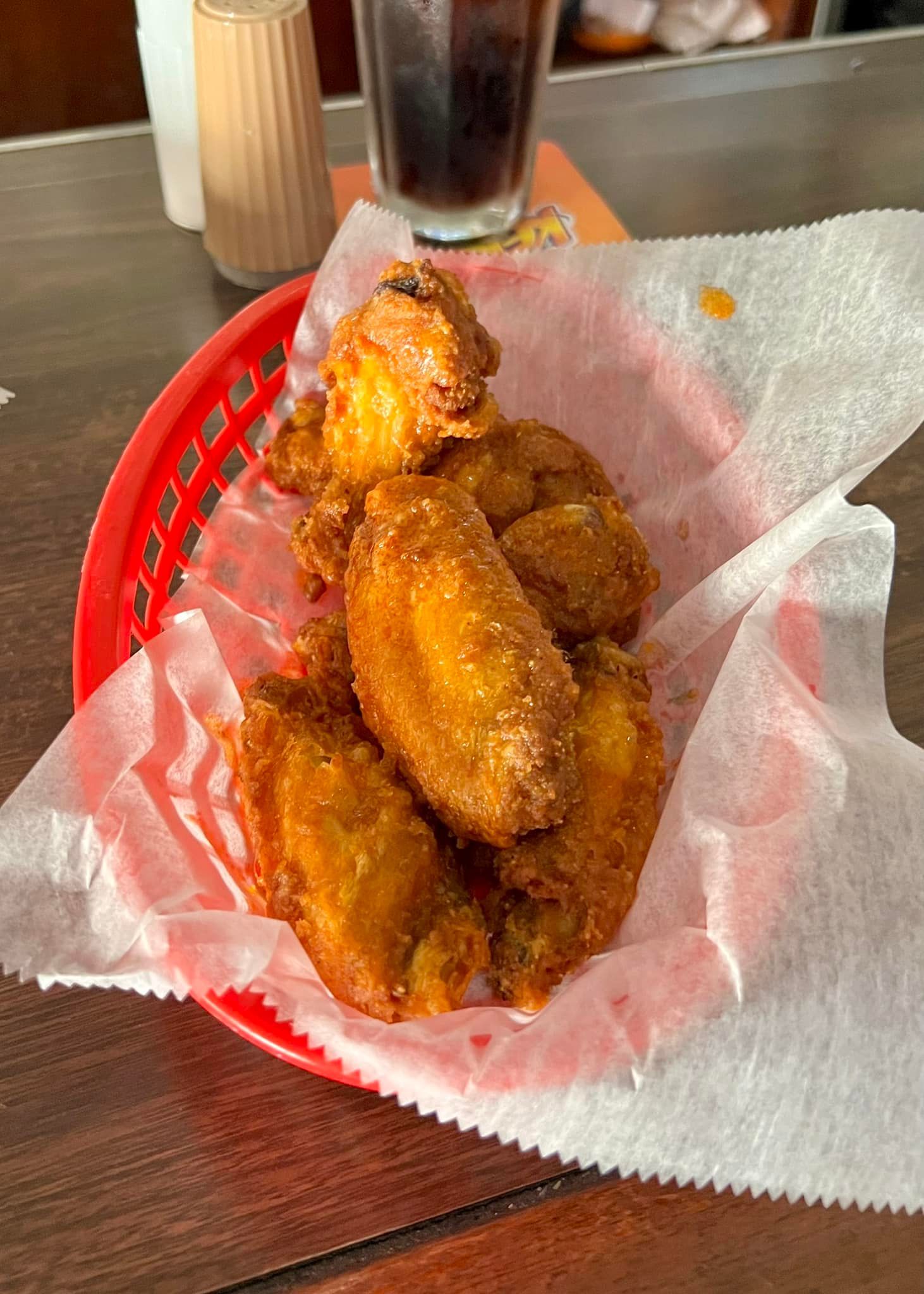 Fried chicken wings in a red basket, lined with paper; a glass of soda is visible.