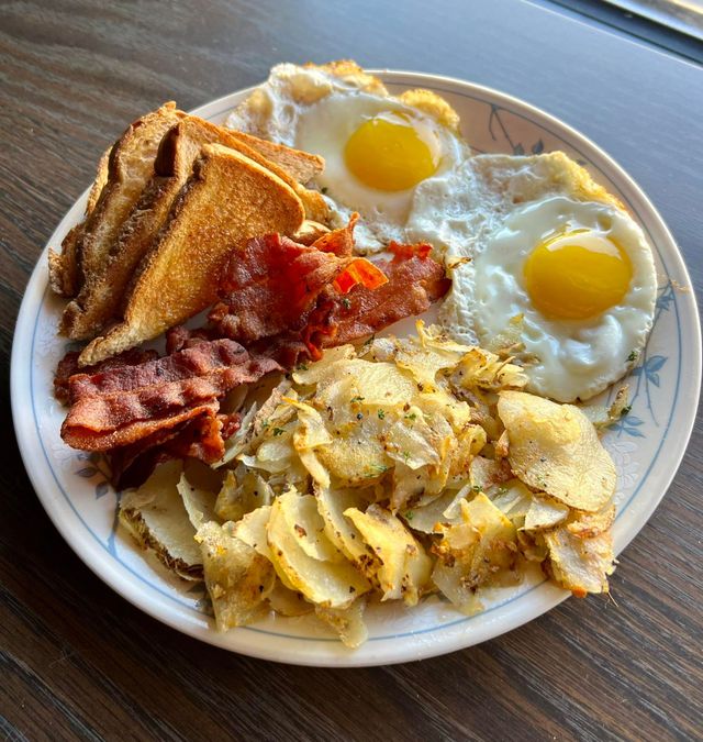 Breakfast plate with fried eggs, bacon, toast, and potato hash.