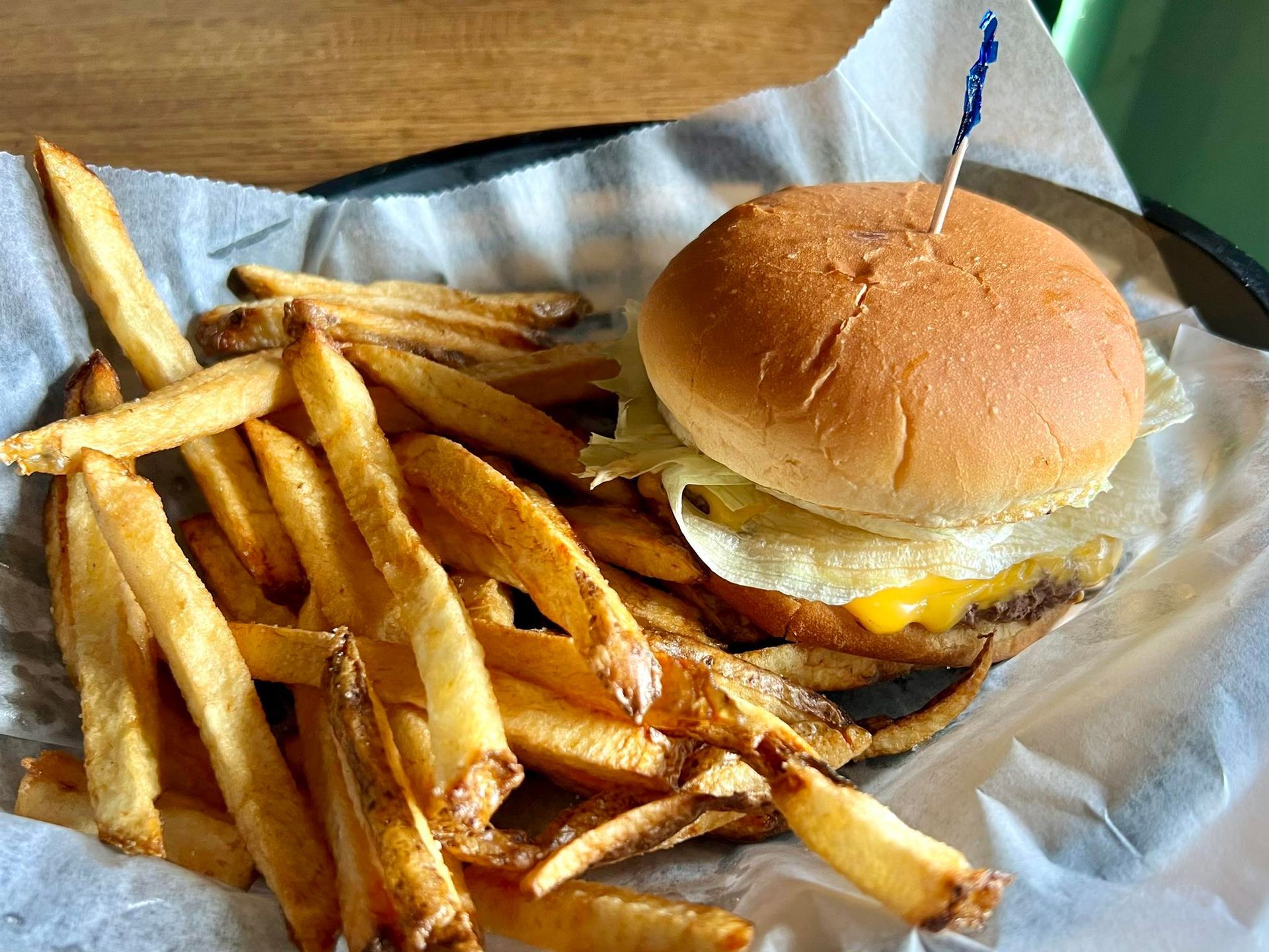 Burger with fries in a basket, on a table. The burger has a toothpick.